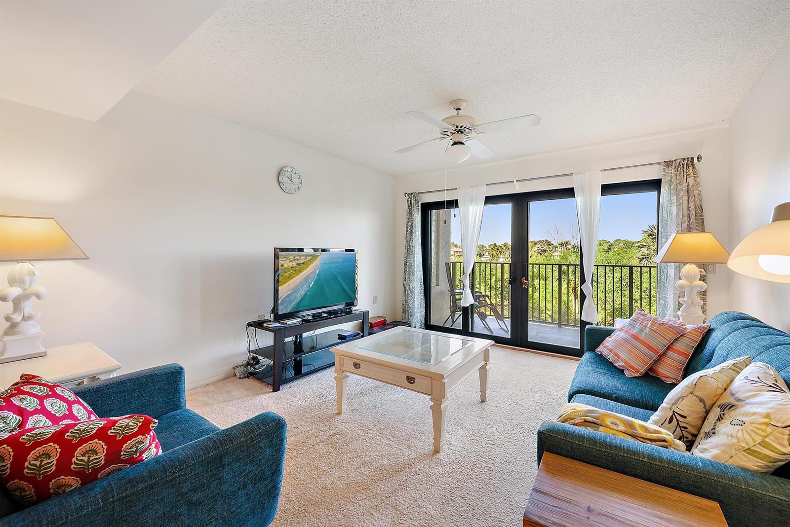 A living room features blue sofas, a coffee table, a television, and a balcony view — 1701 Marina Isle Way # 202, Jupiter FL 33477, JUPITER, FL