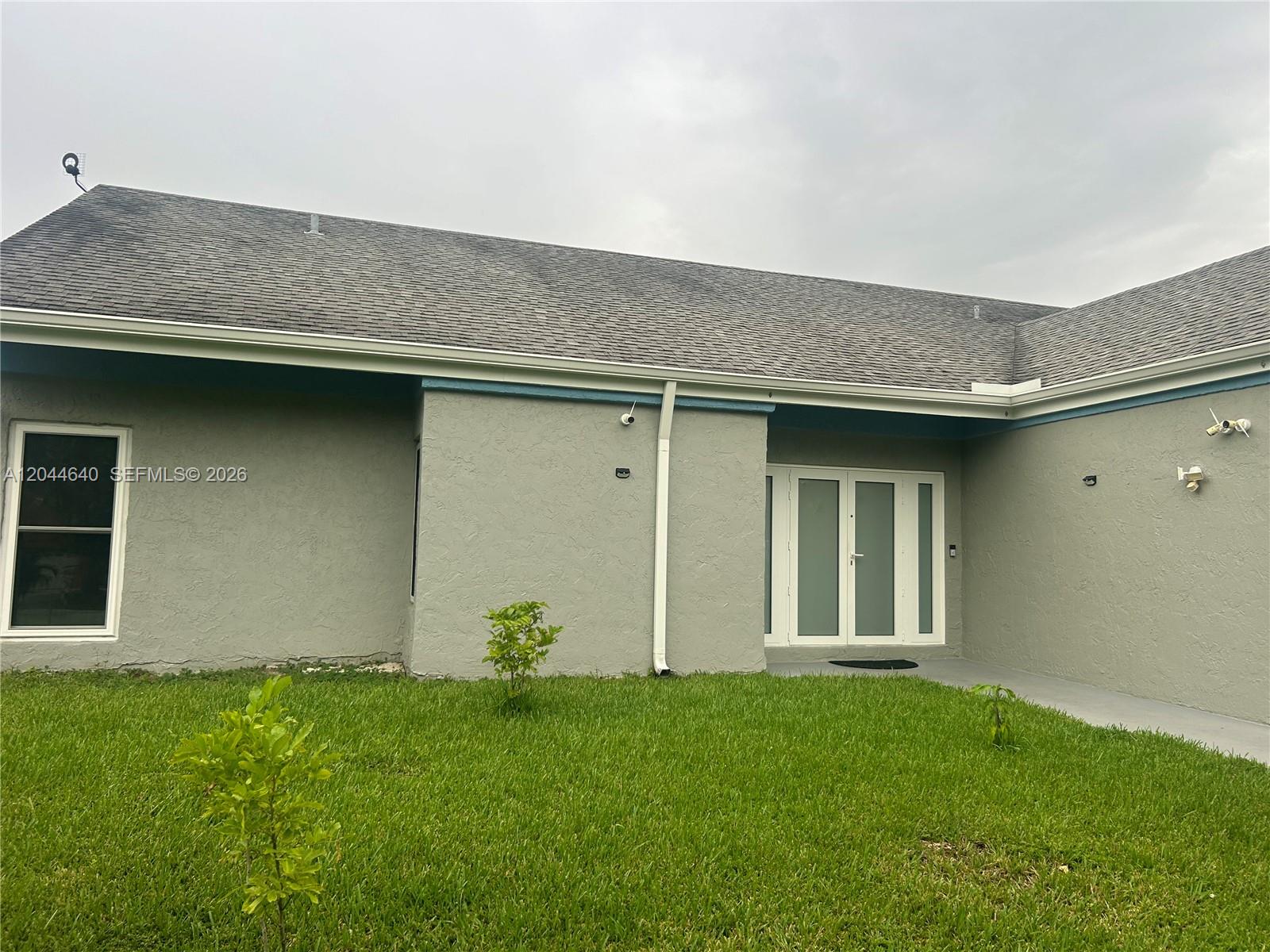 The exterior of a gray stucco house features a shingled roof and double glass doors — 2730 Cypress Ave, Miramar FL 33025, MIRAMAR, FL