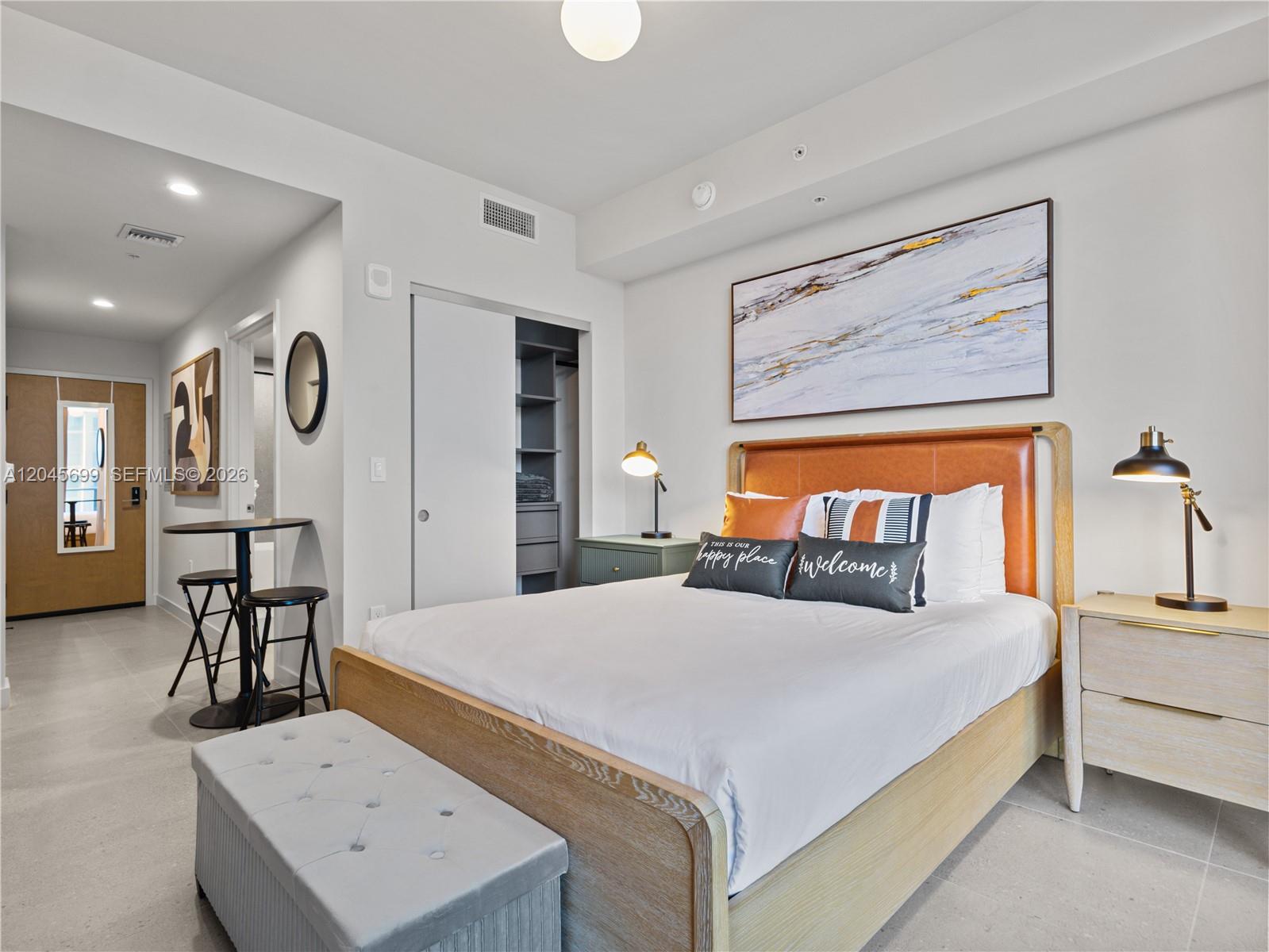 A bedroom features a bed with a leather headboard, a bench, and a small dining area — 11 NE 6th St # 2102, Miami FL 33132, MIAMI, FL