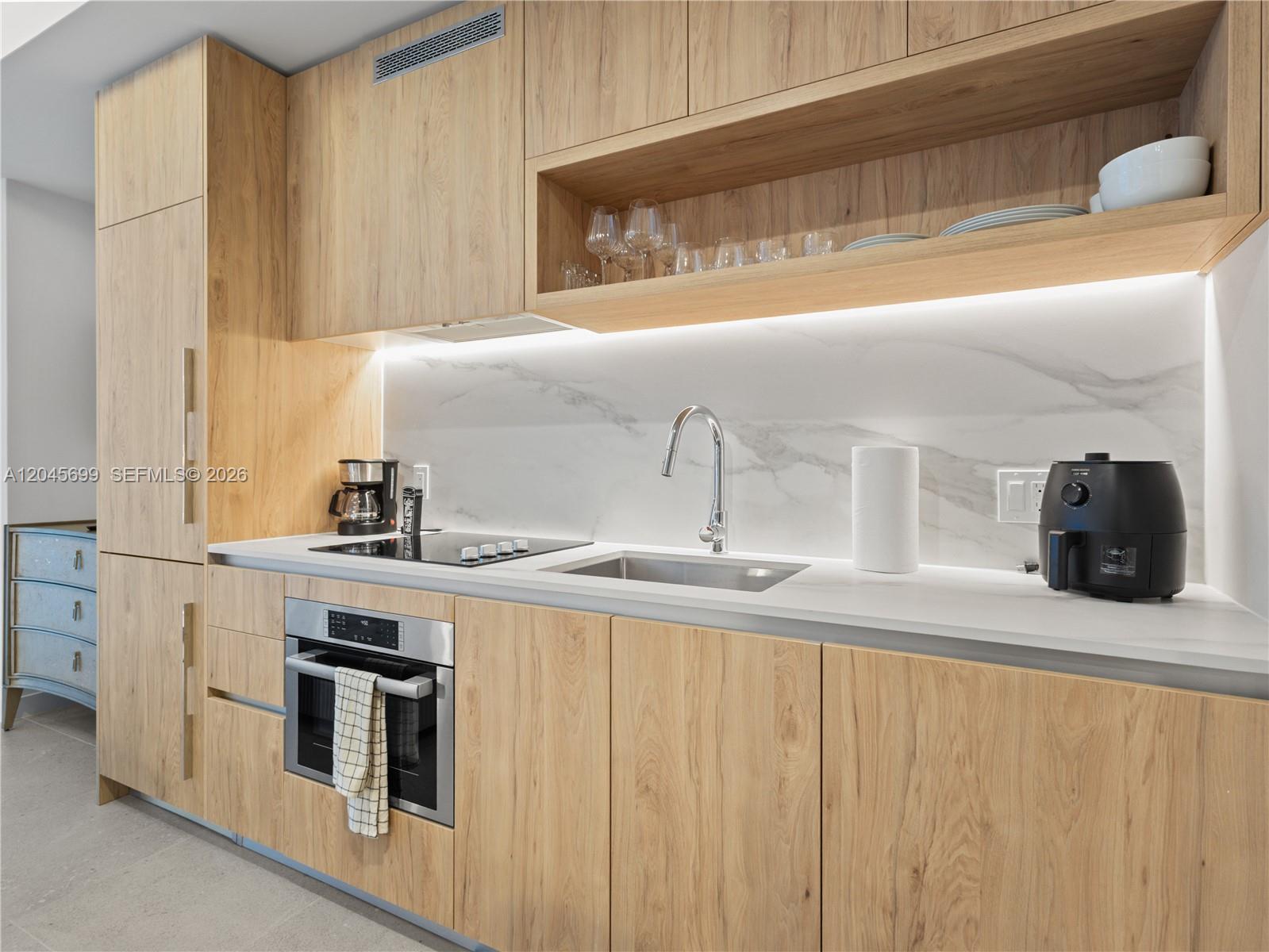 A modern kitchen features light wood cabinetry, a marble backsplash, and stainless steel appliances — 11 NE 6th St # 2102, Miami FL 33132, MIAMI, FL