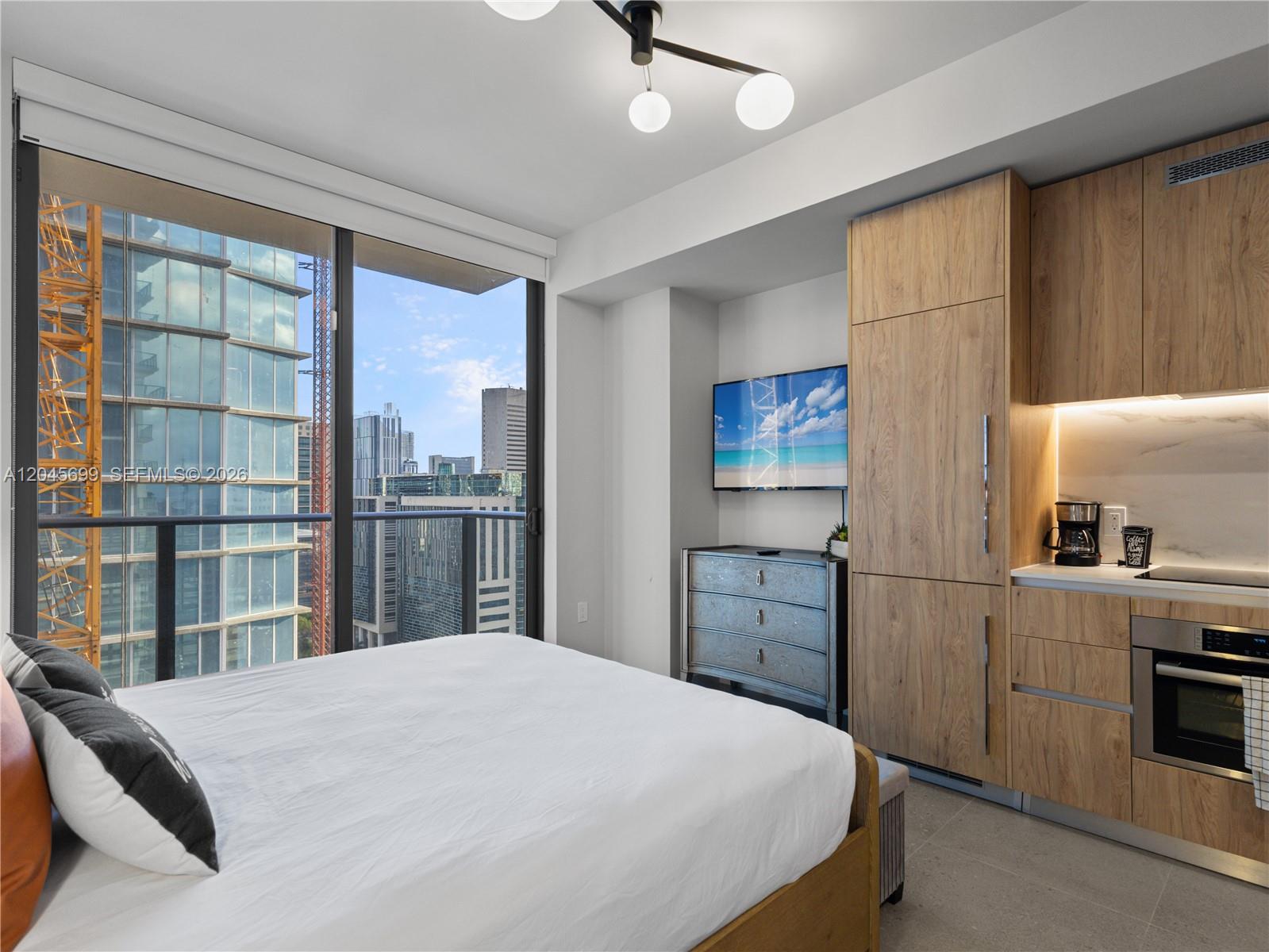 A bedroom features a bed, a wall-mounted television, and a kitchenette with wood-toned cabinetry — 11 NE 6th St # 2102, Miami FL 33132, MIAMI, FL