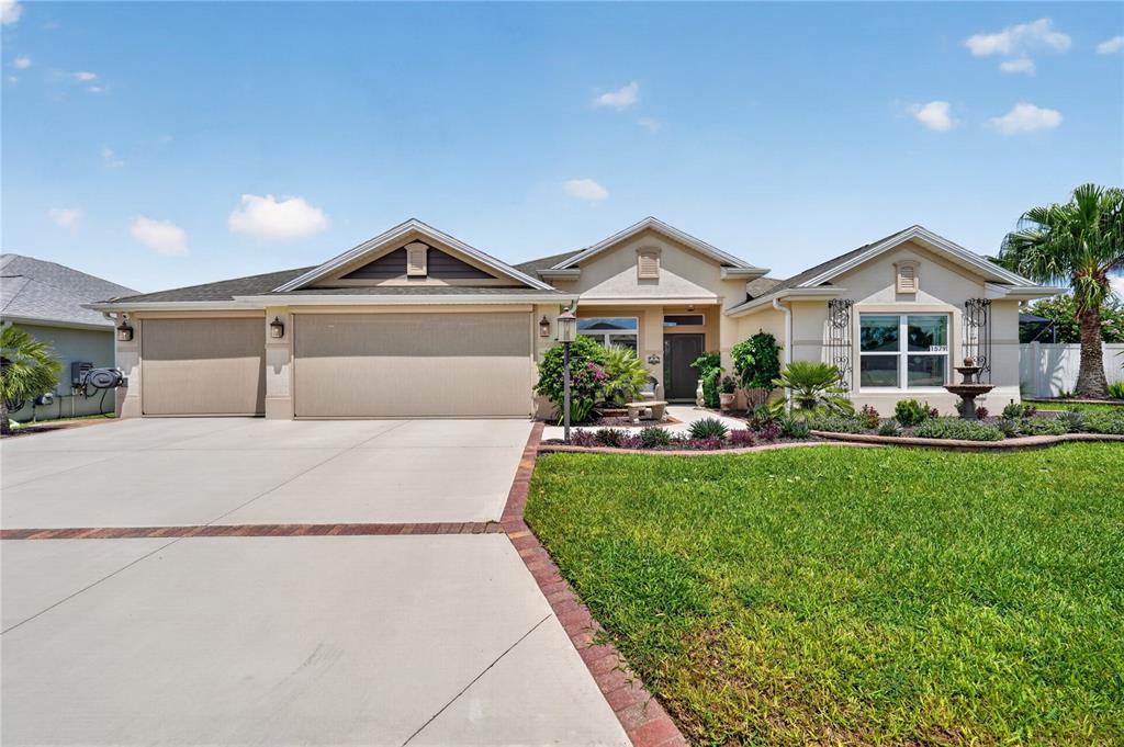 A single-story house with a three-car garage, beige stucco exterior, and a landscaped front yard — 1579 MCELDOWNEY PLACE, THE VILLAGES, FL