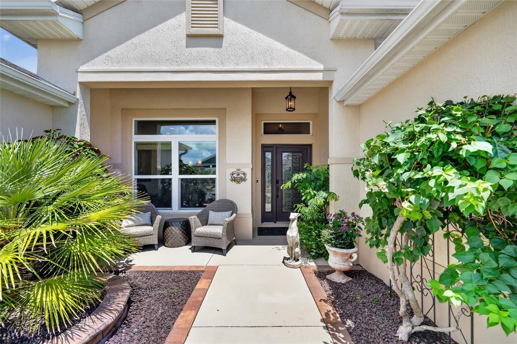 A front entryway features a concrete walkway, two wicker chairs, and lush landscaping — 1579 MCELDOWNEY PLACE, THE VILLAGES, FL
