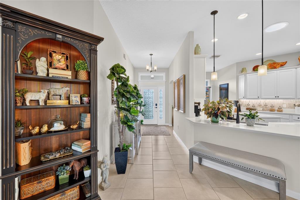 A hallway leads to a front door, featuring a tall bookshelf and a kitchen counter — 1579 MCELDOWNEY PLACE, THE VILLAGES, FL