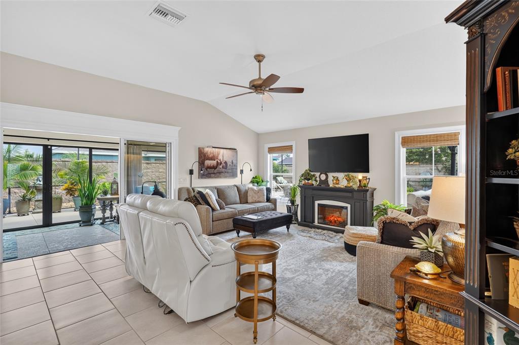 A living room features a fireplace, a ceiling fan, and sliding doors leading to a patio — 1579 MCELDOWNEY PLACE, THE VILLAGES, FL