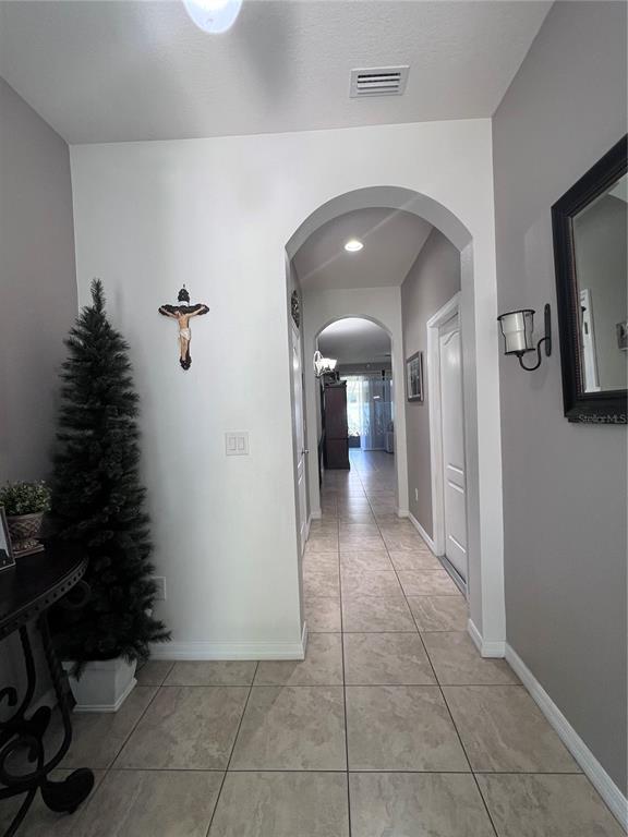 A tiled hallway features arched doorways, gray walls, and a crucifix on the wall — 10426 YELLOW SPICE COURT, RIVERVIEW, FL