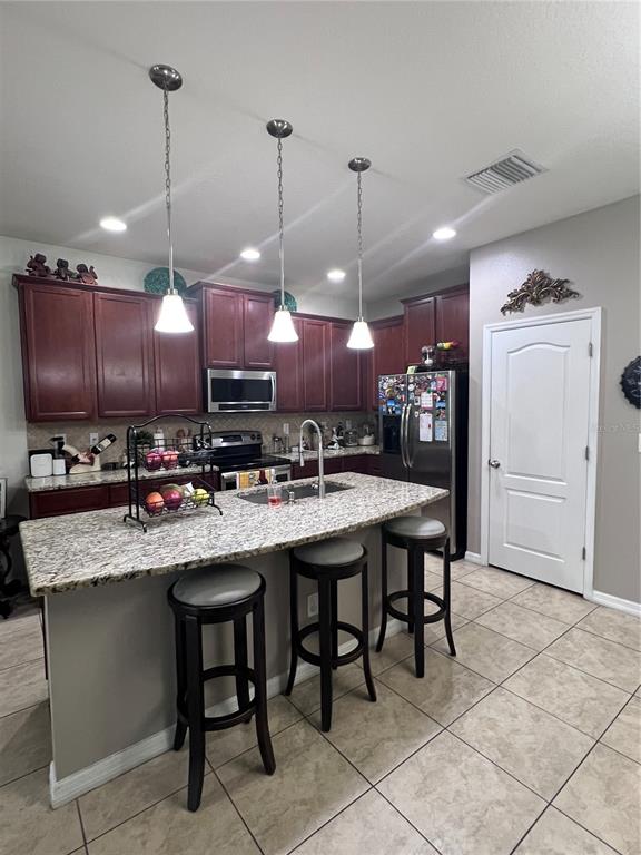 A kitchen features dark wood cabinets, granite countertops, a center island with stools, and stainless appliances — 10426 YELLOW SPICE COURT, RIVERVIEW, FL