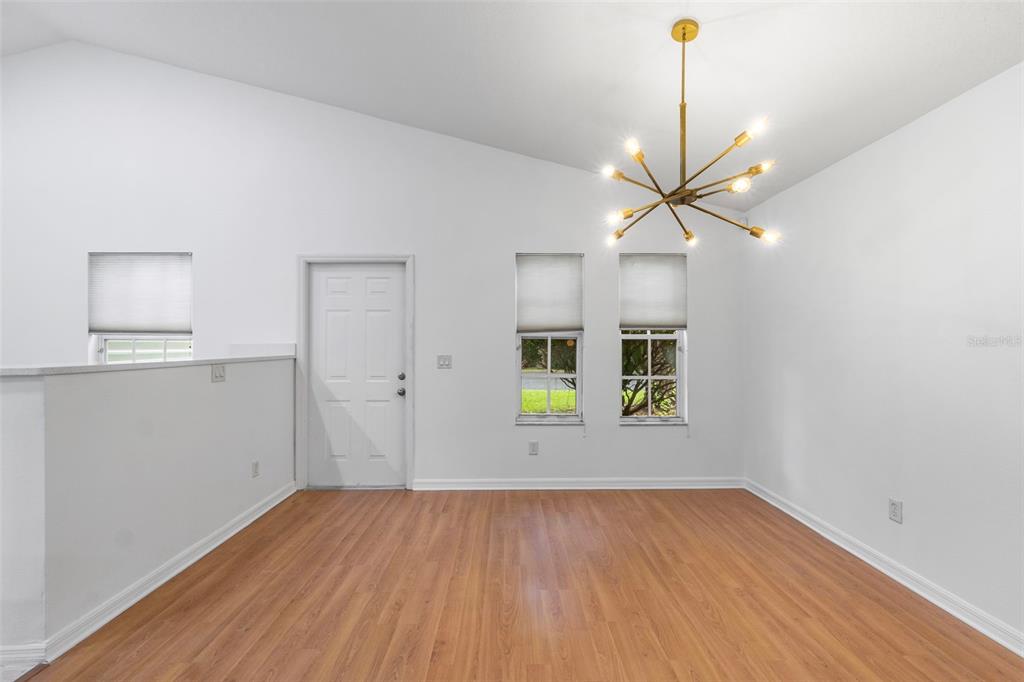 An empty room with wood-look flooring, a vaulted ceiling, a modern chandelier, and three windows — 287 MARSH LANDING CIRCLE, DEBARY, FL