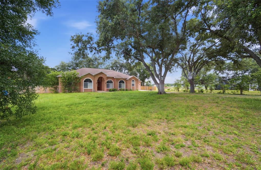 A single-story house with a tan exterior sits on a large, grassy lot with trees — 6611 W KNIGHTS GRIFFIN ROAD, PLANT CITY, FL