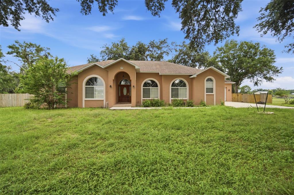 A single-story tan house with arched windows and a central front entrance sits on grass — 6611 W KNIGHTS GRIFFIN ROAD, PLANT CITY, FL