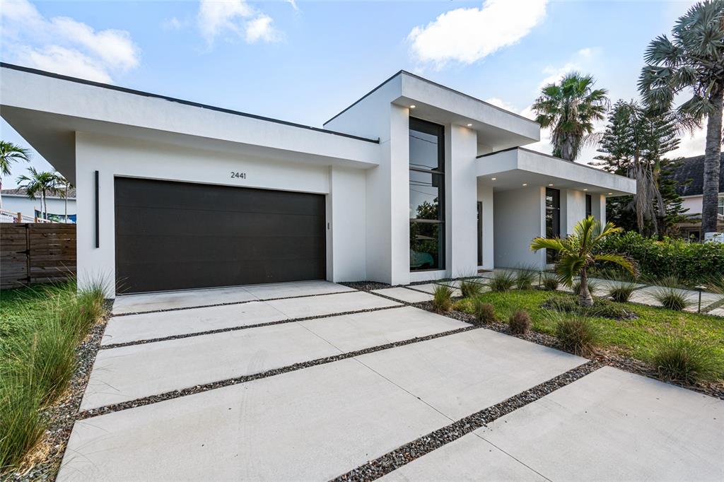 A modern white house features a dark garage door and a concrete driveway with gravel — 2441 WEBBER STREET, SARASOTA, FL