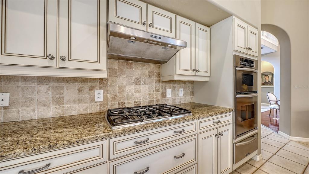 A kitchen features white cabinetry, granite countertops, a gas cooktop, and a stainless steel oven — 4839 SWEETMEADOW CIRCLE, SARASOTA, FL