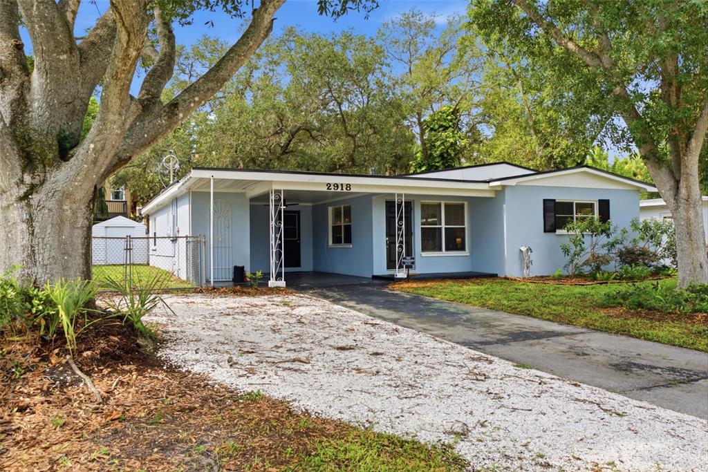 A light blue single-story house features a gravel driveway, a carport, and mature trees — 2918 W ELLIS DRIVE, TAMPA, FL