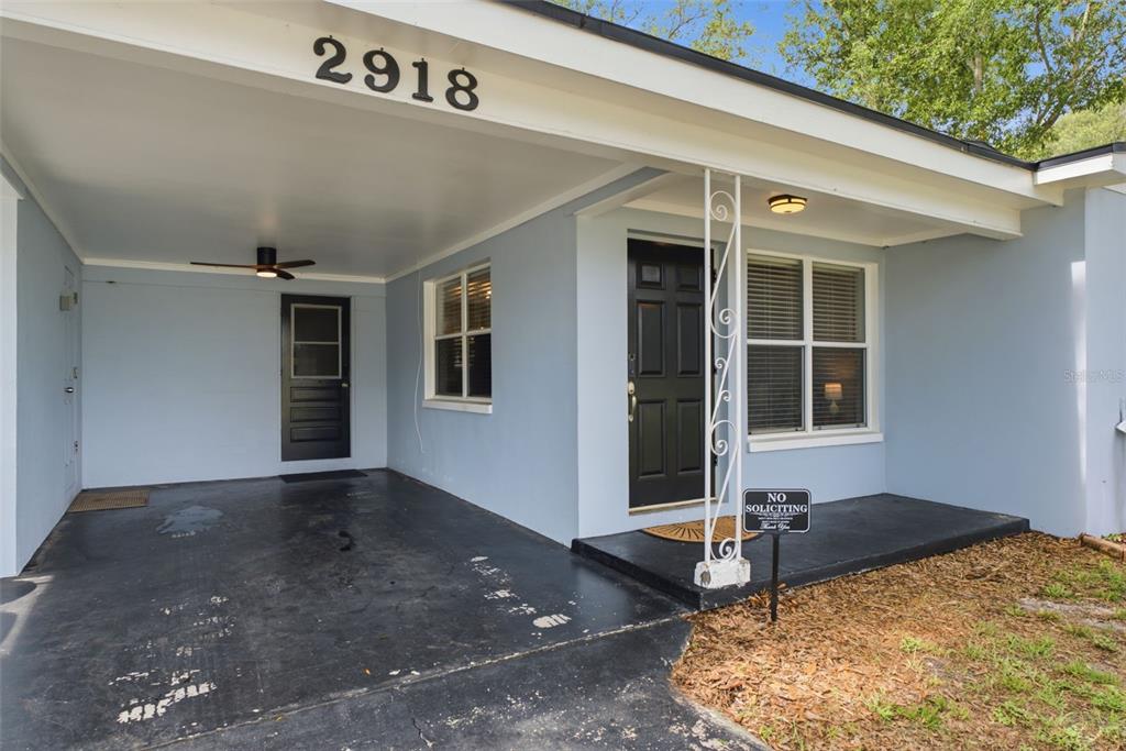 A light blue house exterior features a covered carport, black doors, and a front porch — 2918 W ELLIS DRIVE, TAMPA, FL