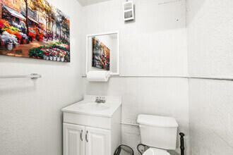 A small bathroom features a white vanity, a toilet, a mirror, and wall-mounted artwork — 1791 Blount Road # 814, Pompano Beach FL 33069, POMPANO BEACH, FL