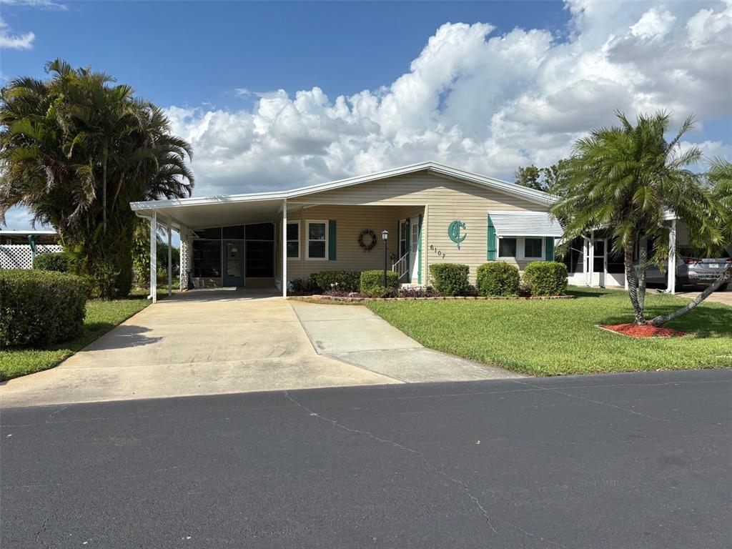 A single-story house with a carport, tan siding, and a manicured lawn — 6107 GRAND OAKS DRIVE SE, WINTER HAVEN, FL