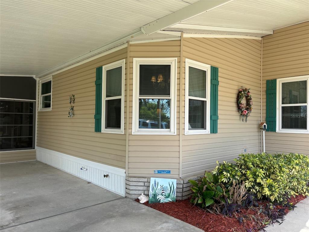 The exterior of a manufactured home features beige vinyl siding, green shutters, and a carport — 6107 GRAND OAKS DRIVE SE, WINTER HAVEN, FL