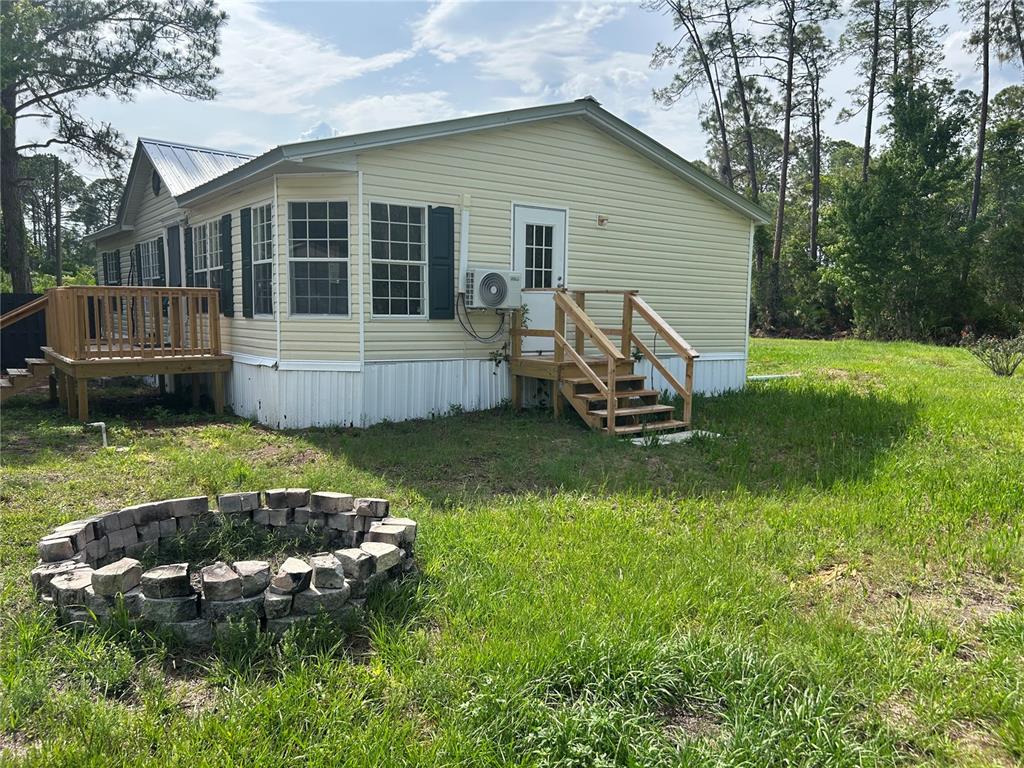 A light-yellow manufactured home features a wooden deck, a back staircase, and a stone firepit — 2585 VISTA PARK DRIVE, DELAND, FL