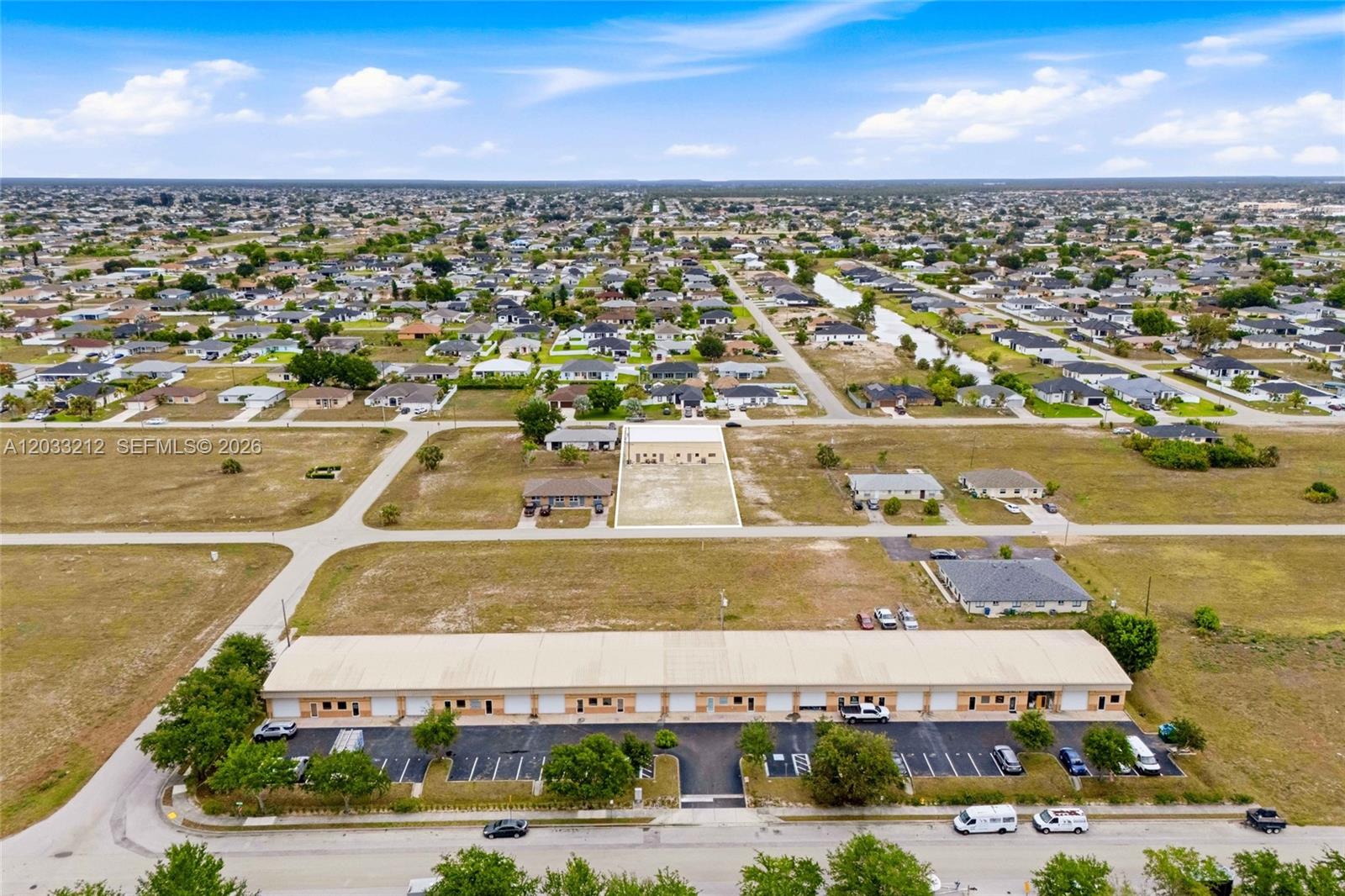 An aerial view shows a commercial warehouse building and a vacant lot in a residential area — CAPE CORAL, FL