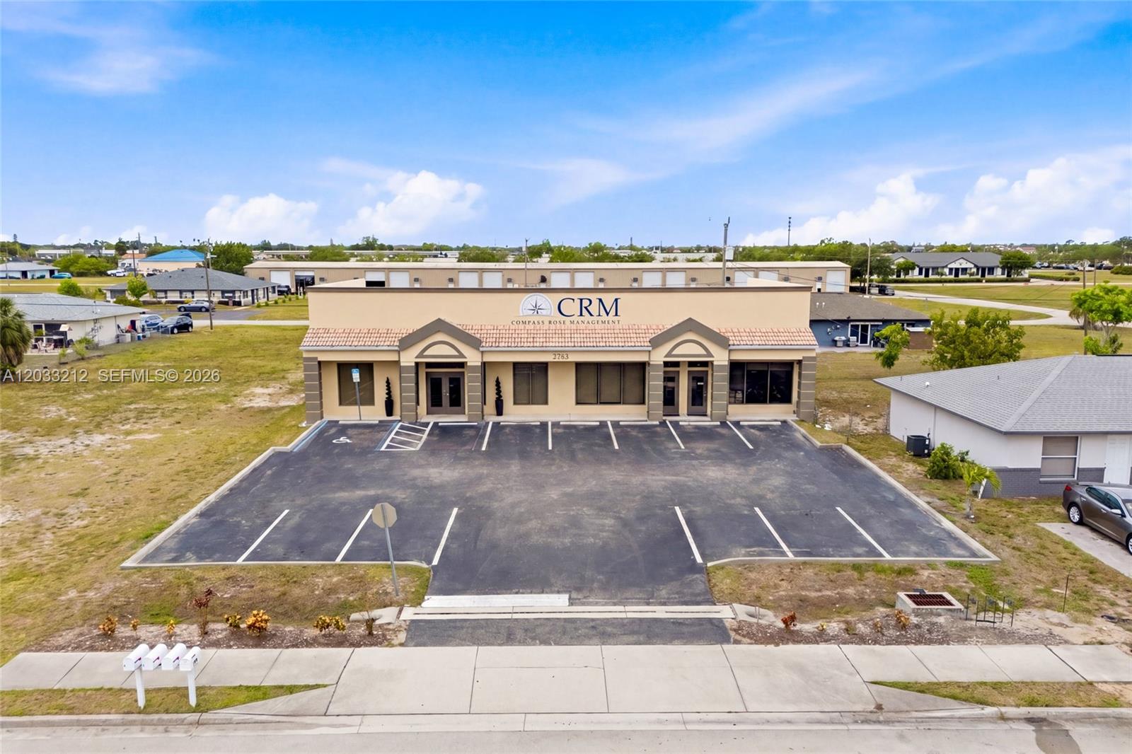 An aerial view shows a commercial building with a parking lot and a tan facade — CAPE CORAL, FL