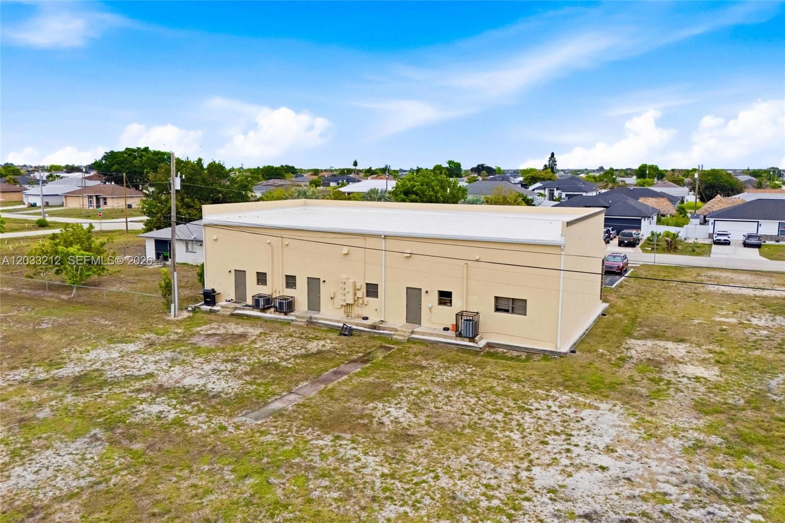 An aerial view shows the exterior of a beige, flat-roofed commercial building on a lot — CAPE CORAL, FL