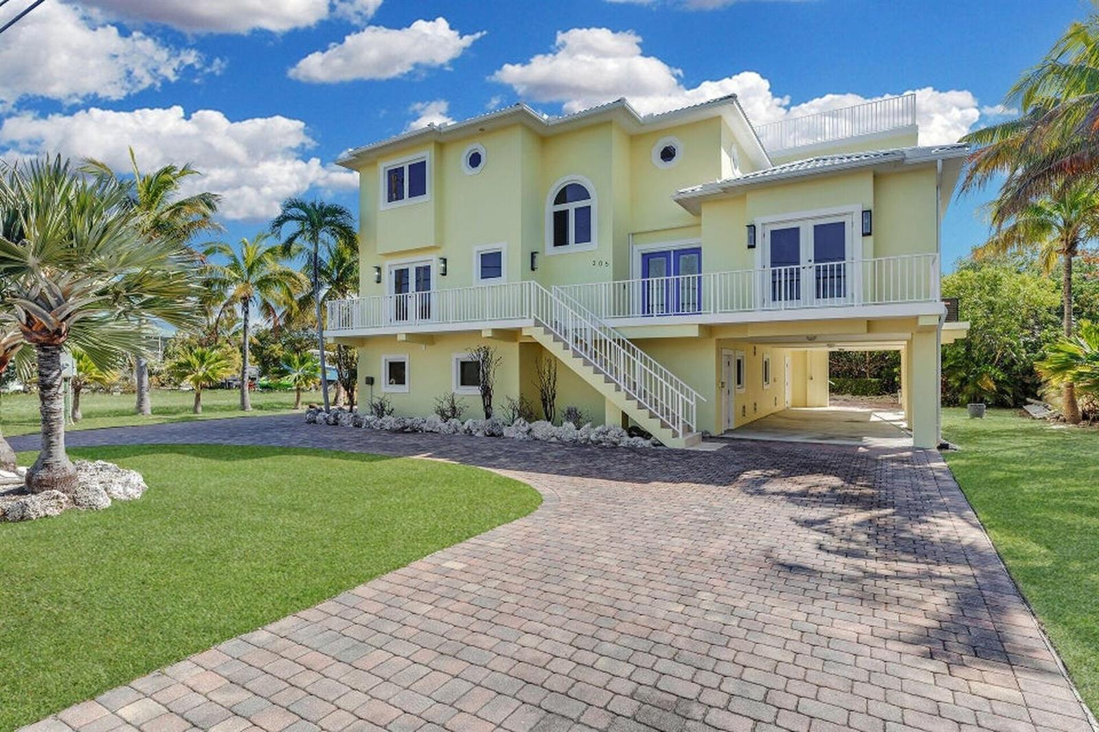 A yellow three-story house with a raised main floor, white railings, and a paved driveway — 205 Stirrup Key Boulevard, Marathon FL 33050, MARATHON, FL