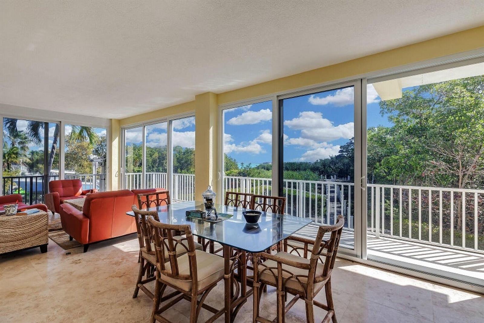 A sunroom with a glass dining table, rattan chairs, red sofa, and large sliding glass doors — 205 Stirrup Key Boulevard, Marathon FL 33050, MARATHON, FL