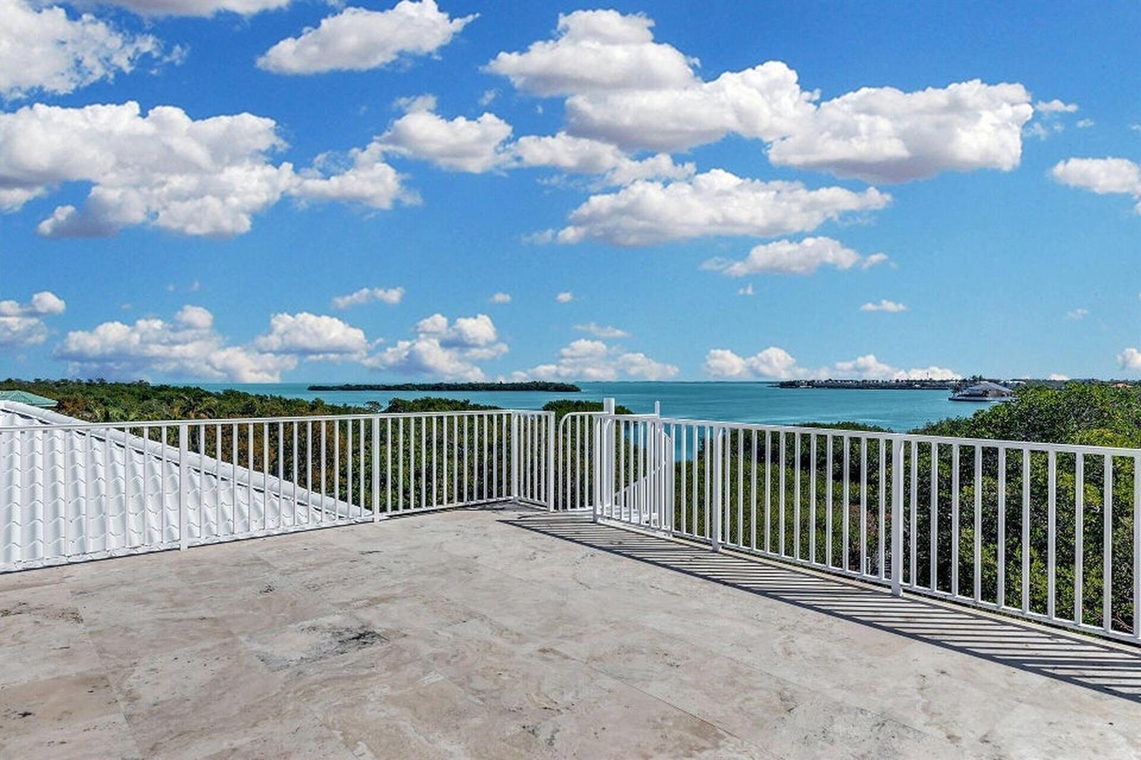 A rooftop terrace with white railings overlooks a body of water and lush green trees — 205 Stirrup Key Boulevard, Marathon FL 33050, MARATHON, FL