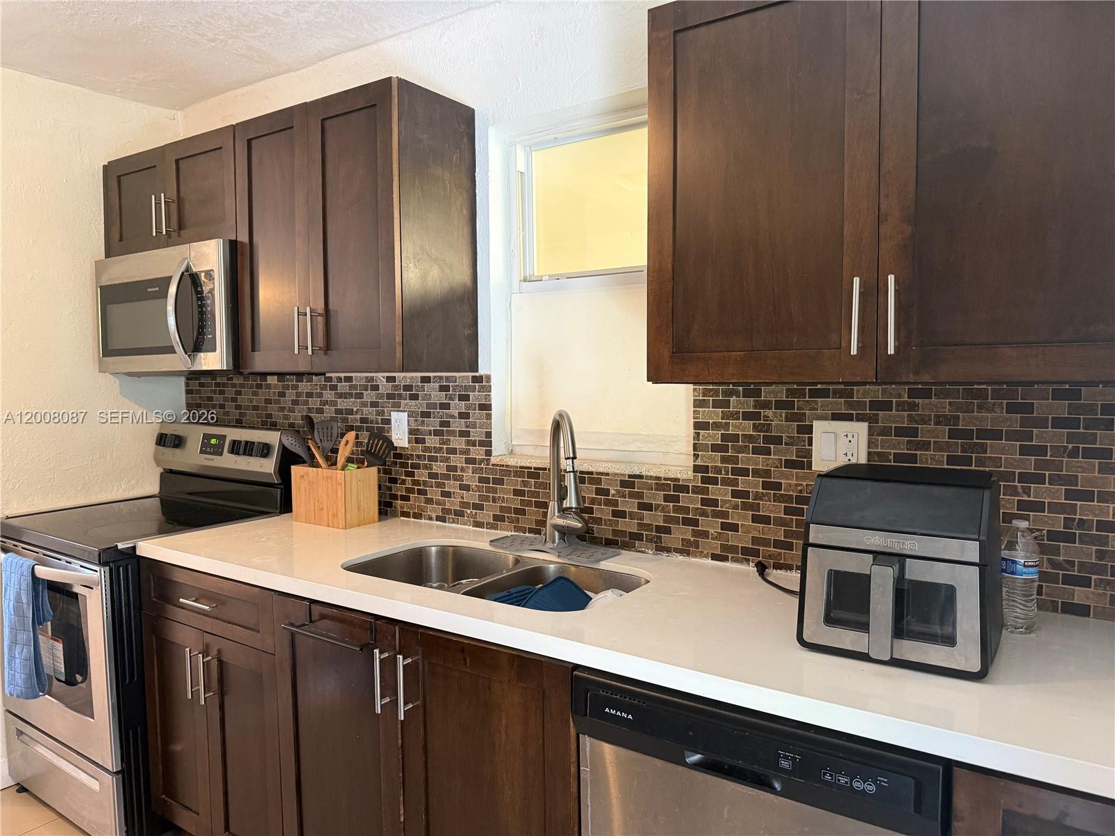 A kitchen features dark wood cabinets, a white countertop, stainless steel appliances, and a tiled backsplash — 2323 Cleveland St, Hollywood FL 33020, HOLLYWOOD, FL