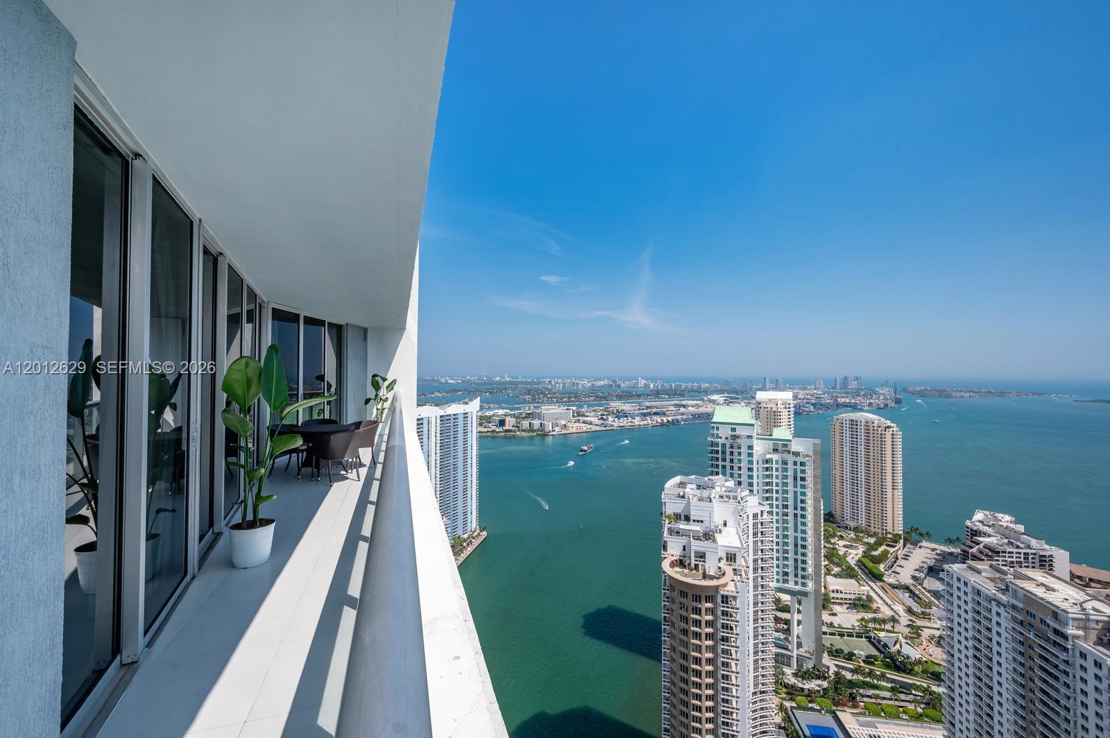 A high-rise balcony overlooks a bay with multiple skyscrapers and a clear blue sky — 465 E Brickell Ave # 5305, Miami FL 33131, MIAMI, FL