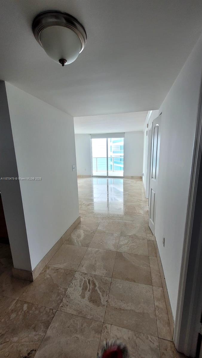 A hallway with light-colored tile flooring leads to a living area with a glass balcony door — 2101 Brickell Ave # 1109, Miami FL 33129, MIAMI, FL