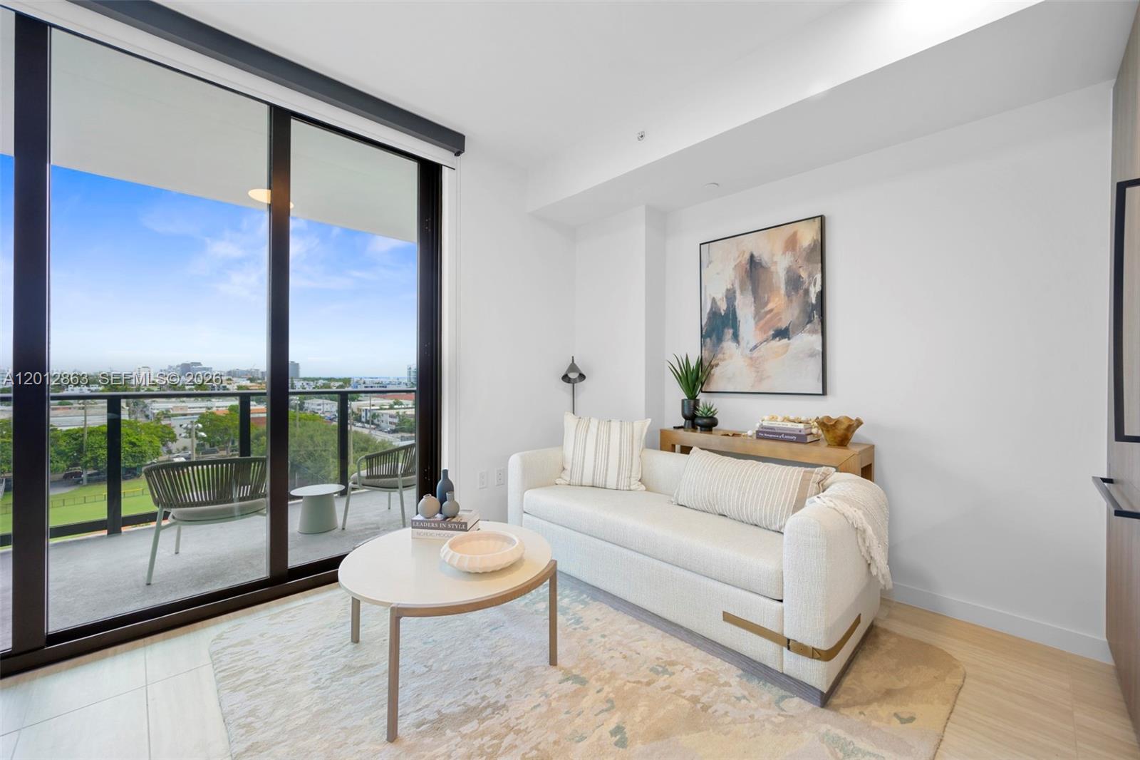A modern living room features a white sofa, round coffee table, and balcony access — 580 72nd St # 611, Miami Beach FL 33141, MIAMI BEACH, FL