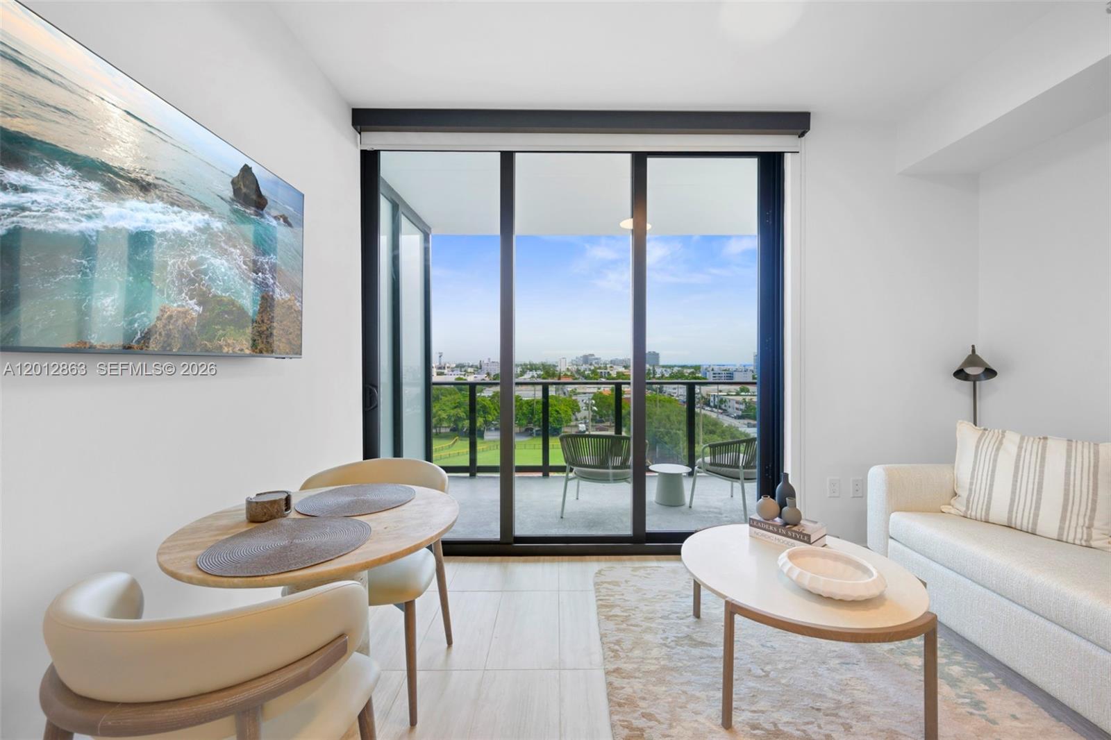 A modern living and dining area features a balcony with city views and tile flooring — 580 72nd St # 611, Miami Beach FL 33141, MIAMI BEACH, FL
