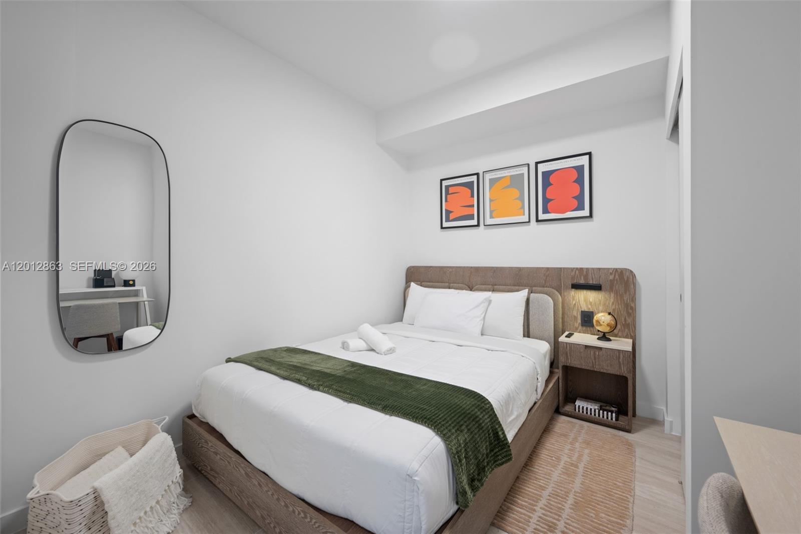 A bedroom features a bed with a green throw, a wooden headboard, and wall art — 580 72nd St # 611, Miami Beach FL 33141, MIAMI BEACH, FL