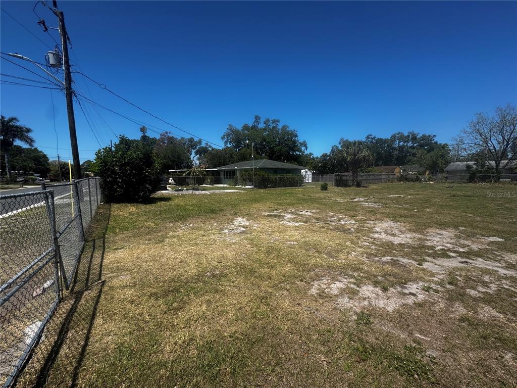A vacant, grassy lot is enclosed by a chain-link fence with a house in the background — 121 33RD AVENUE E, BRADENTON, FL