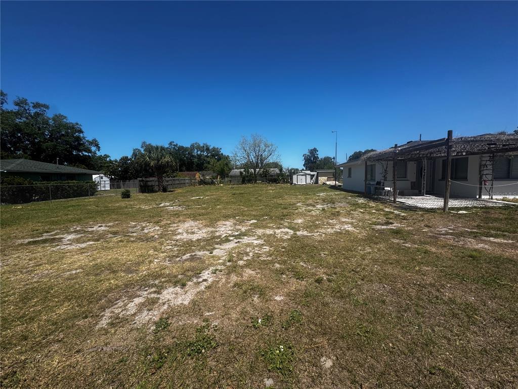A large, grassy backyard features patches of sand and a covered patio attached to a house — 121 33RD AVENUE E, BRADENTON, FL