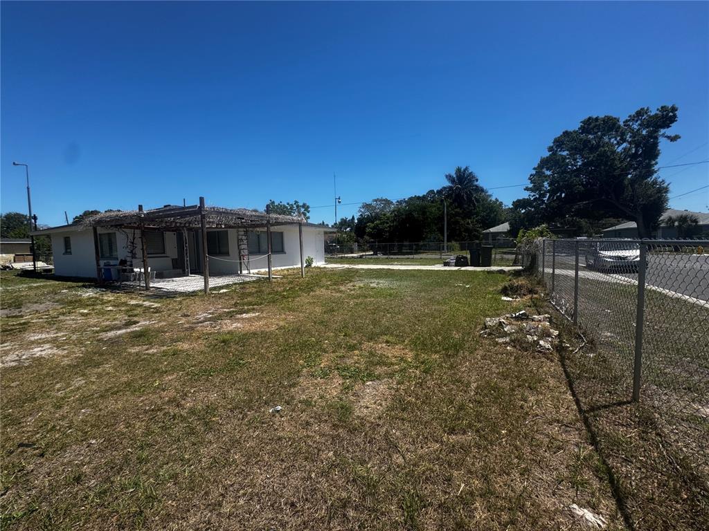 A white house with a wooden pergola stands on a grassy lot beside a fence — 121 33RD AVENUE E, BRADENTON, FL