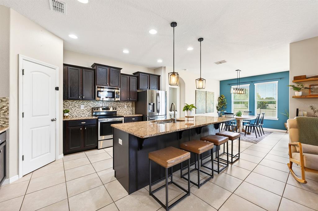 A kitchen features dark wood cabinets, granite countertops, a central island, and an adjacent dining area — 4062 BROOKSHIRE CIRCLE, EUSTIS, FL