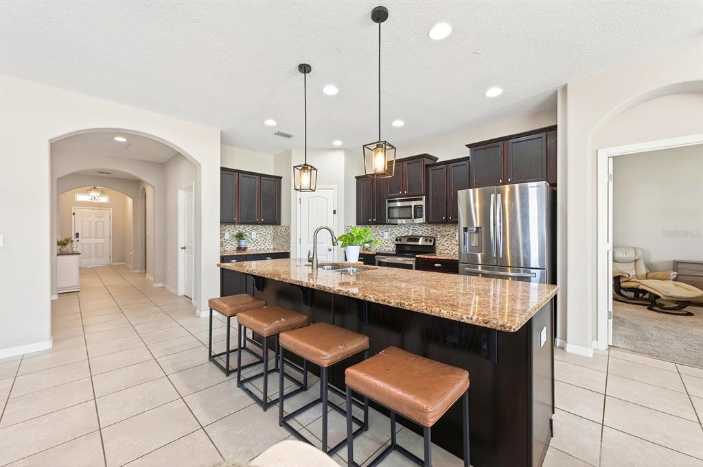 A kitchen features dark wood cabinets, granite countertops, a central island with stools, and tile flooring — 4062 BROOKSHIRE CIRCLE, EUSTIS, FL