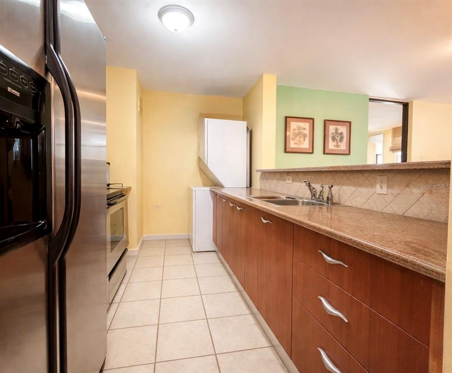 A kitchen features wood cabinets, granite countertops, stainless steel appliances, and light-colored tile flooring — 614 NE BEACHSIDE DRIVE UNIT 205, LUQUILLO, PR
