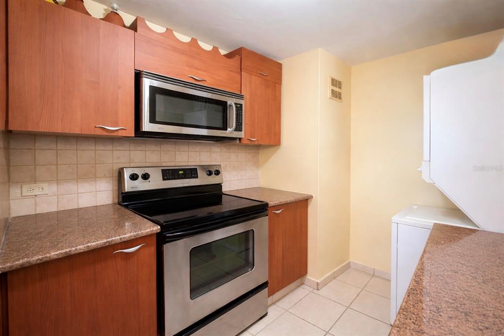 A kitchen features wood cabinets, stainless steel appliances, granite countertops, and a white laundry unit — 614 NE BEACHSIDE DRIVE UNIT 205, LUQUILLO, PR
