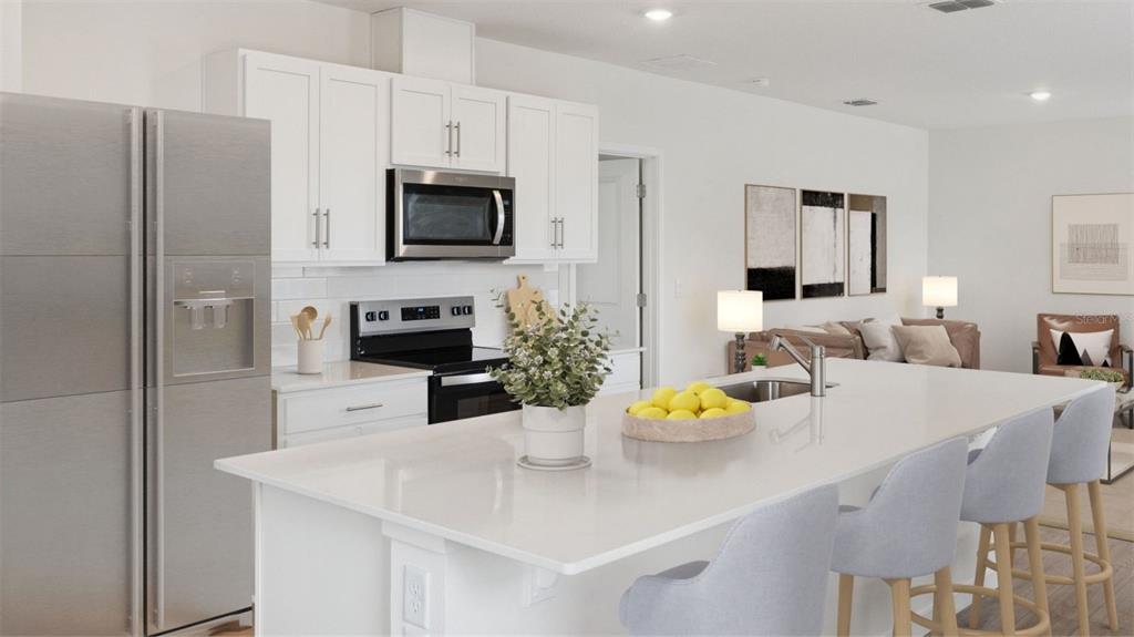A modern kitchen features white cabinetry, stainless steel appliances, and a large quartz-topped island — 5162 BLANKET FLOWER STREET, APOPKA, FL