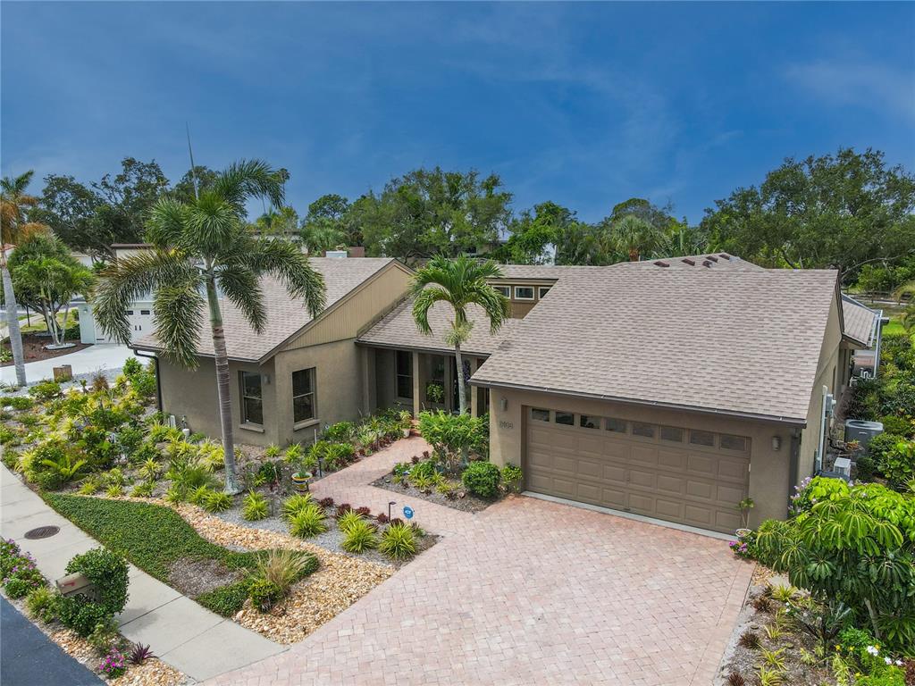 An aerial view shows a tan, single-story house with a shingled roof and paver driveway — 2408 89TH STREET NW, BRADENTON, FL