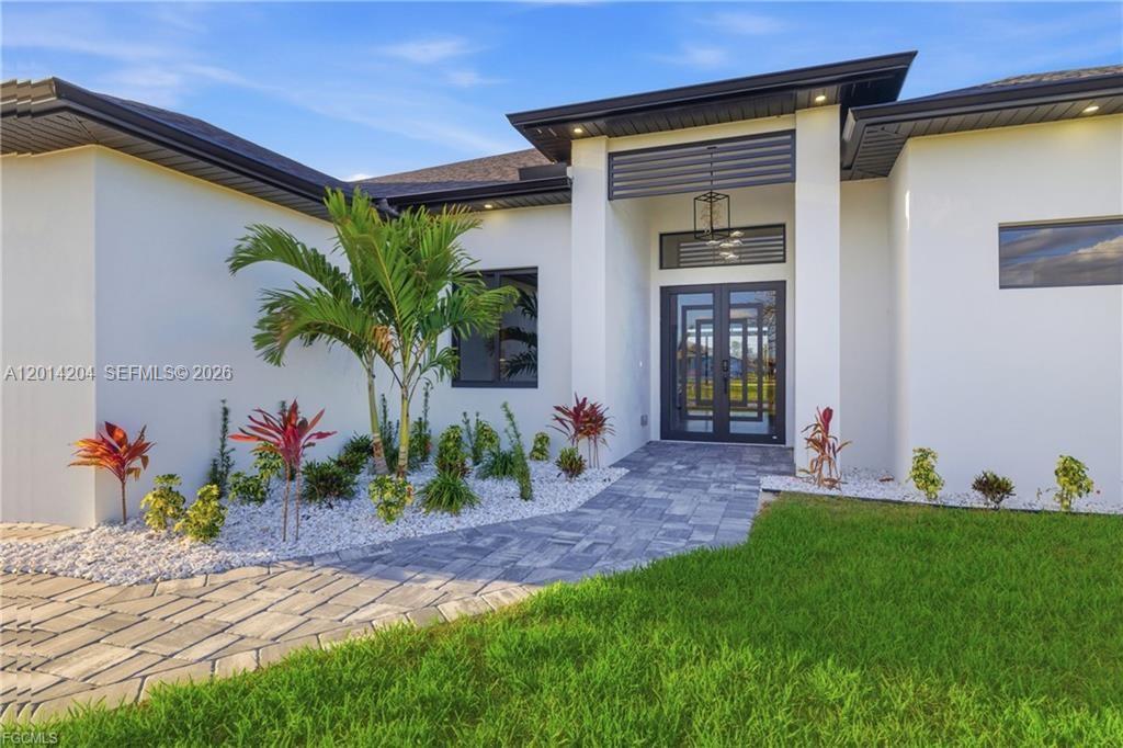 The exterior of a modern white house features a paved walkway and tropical landscaping — 1031 SW 1st TER, Cape Coral FL 33991, CAPE CORAL, FL