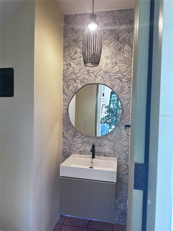 A small bathroom features a floating vanity, a round mirror, and leaf-patterned wallpaper — Carr 115 Km 17 PUNTA DEL MAR D12, RINCON, PR