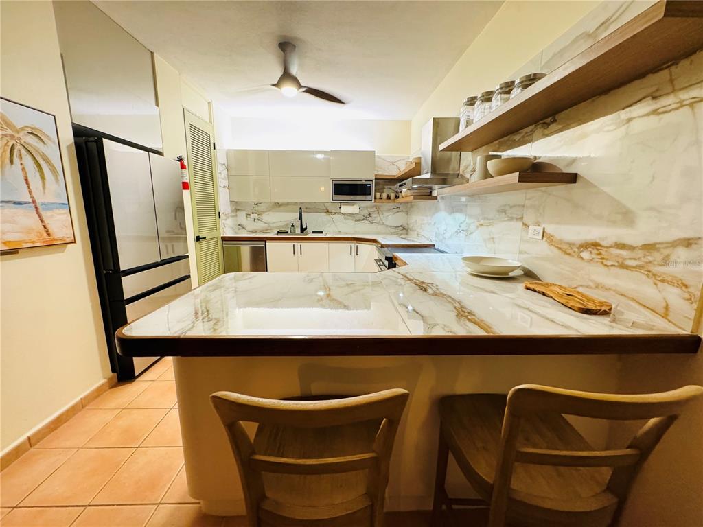 A kitchen features white marble-patterned countertops, wooden floating shelves, and two wooden bar stools — Carr 115 Km 17 PUNTA DEL MAR D12, RINCON, PR