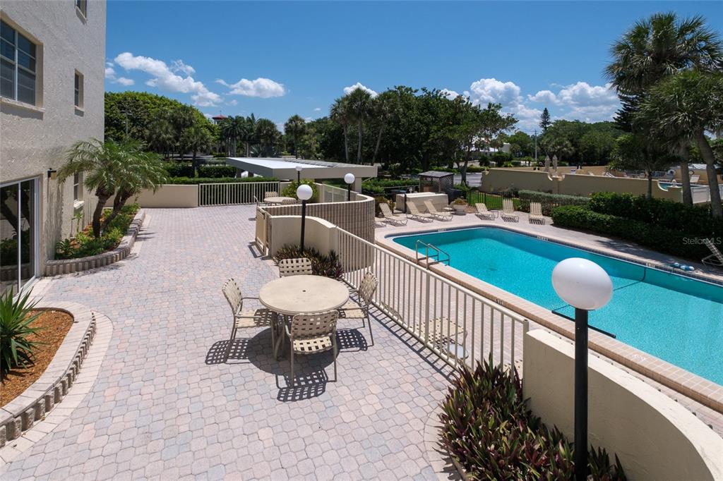 An outdoor patio with a dining set overlooks a swimming pool and landscaped grounds — 4325 GULF OF MEXICO DRIVE UNIT 507, LONGBOAT KEY, FL