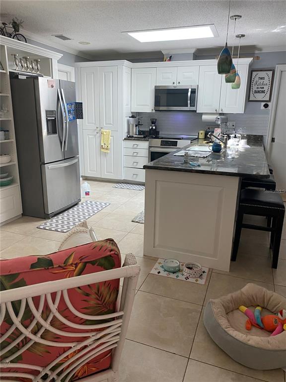 A bright living room features light tile flooring, a grey sofa, and an open kitchen — 1833 OAK VIEW DRIVE, SARASOTA, FL