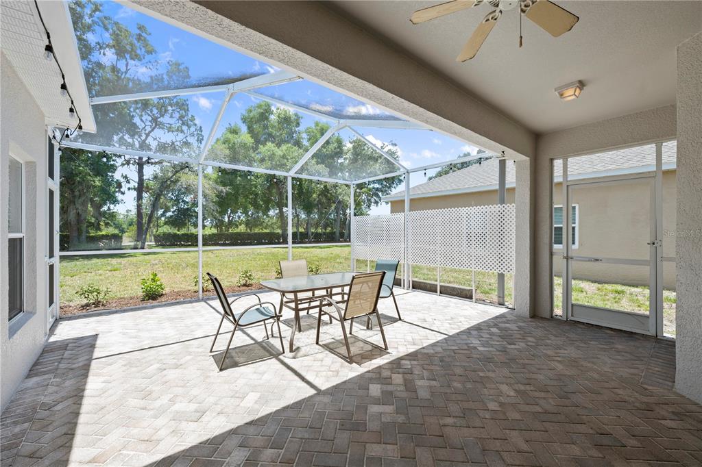 A covered patio features a brick paver floor, a screened enclosure, and outdoor dining furniture — 16712 CARACARA COURT, SPRING HILL, FL