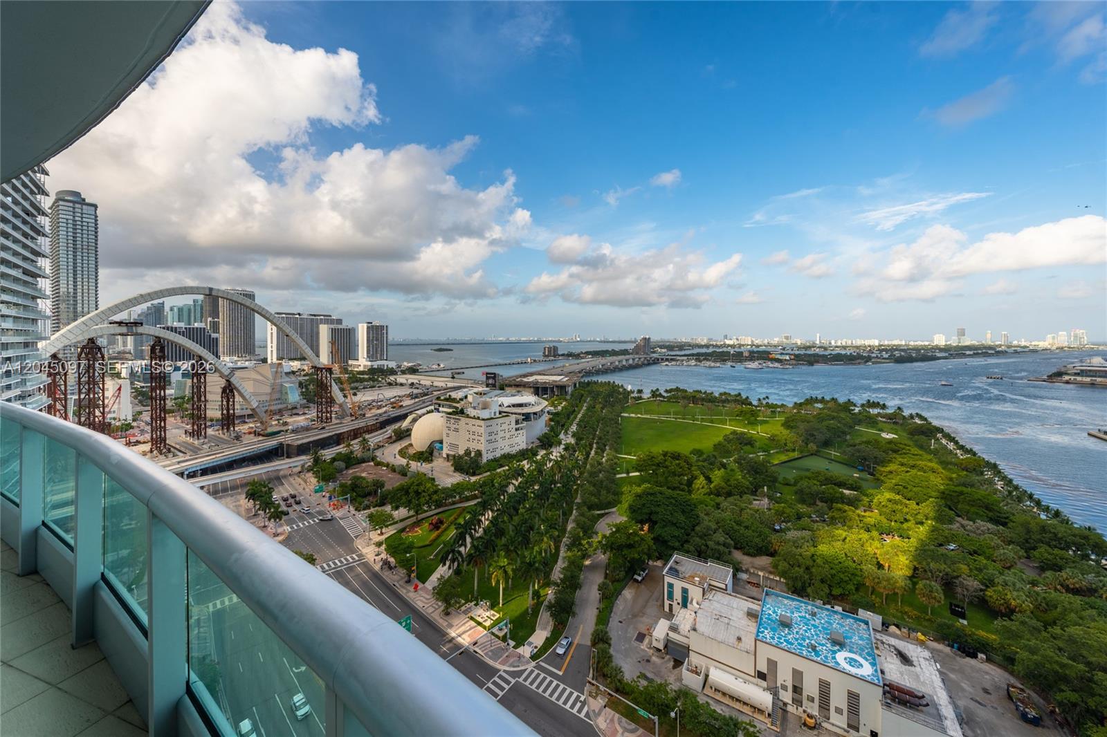 A high-angle view from a balcony overlooks a city park, bridge construction, and the bay — 900 Biscayne Blvd # 2506, Miami FL 33132, MIAMI, FL